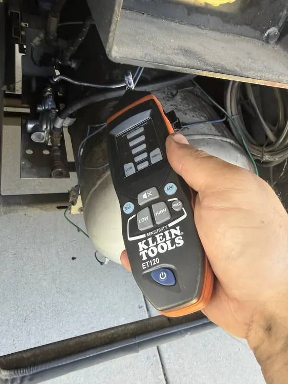 Clamp meter in hand testing a circuit underneath a coach